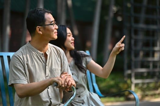 Young woman sitting on a park bench with woman showing something interesting to her father.