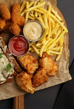 chicken fillet fried in batter with sauce on a wooden board on a black background