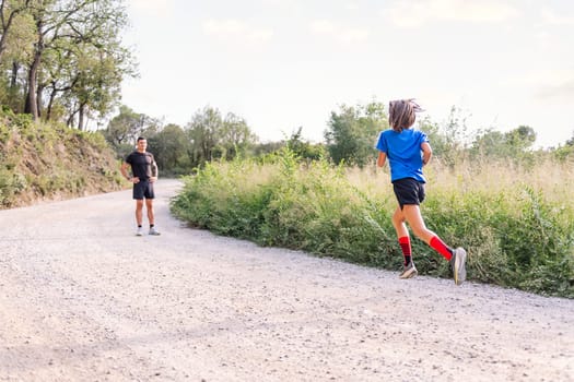 girl running in the countryside while her coach is watching her, concept of sport for kids in nature and active lifestyle, copy space for text