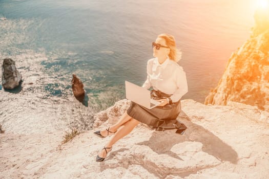 Business woman on nature in white shirt and black skirt. She works with an iPad in the open air with a beautiful view of the sea. The concept of remote work