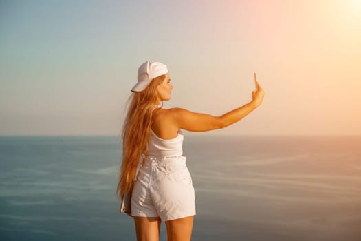 Selfie woman sea. The picture depicts a woman in a cap and tank top, taking a selfie shot with her mobile phone, showcasing her happy and carefree vacation mood against the beautiful sea backgroun.