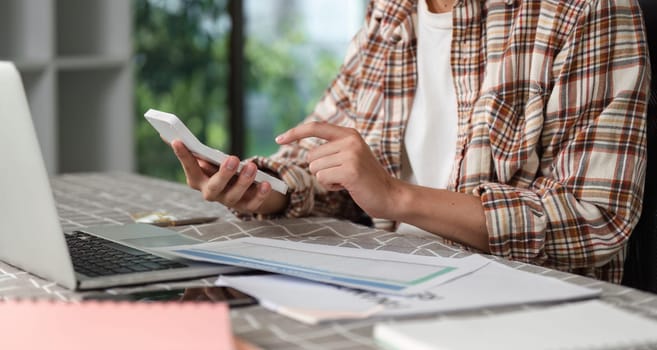 A focused person interacts with a smartphone while reviewing financial documents, highlighting the integration of technology in their work.