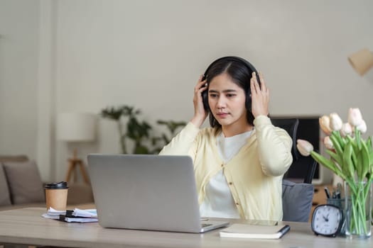 A dedicated freelance businesswoman works from home, wearing headphones and engaged with her laptop, showcasing modern remote work.