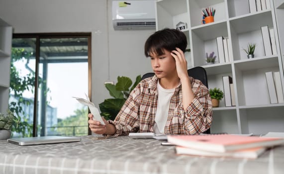 A young man sits in his home office, feeling overwhelmed as he reviews financial documents, showcasing the stress of budgeting and personal finance.