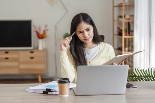A dedicated businesswoman works from home, concentrating on her freelance projects while managing her tasks with a laptop and notes.
