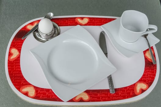 Table place setting breakfast with egg on a red white pad.
