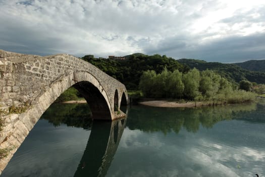 The landscape with the stone bridge of Rijeka Crnojevica with the river Rijeka Crnojevica at the western end of the Skadarsko Jezero lake or Skadar lake in Central Montenegro in Montenegro in the Balkans on the Mediterranean Sea in Europe.