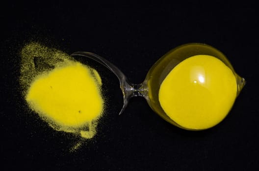 Deadline Concept Broken Hourglass with Yellow Sand on Black Background
