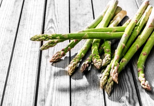 Bunch of fresh uncooked green asparagus spears, shoots or tips lying on a rustic wooden table outdoors with copyspace