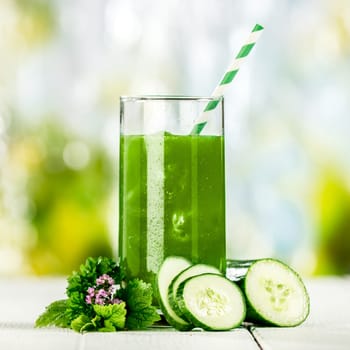 Tasty healthy green vegetable juice with cucumber blended from fresh ingredients and served in a tall glass on a table outdoors in a summer garden