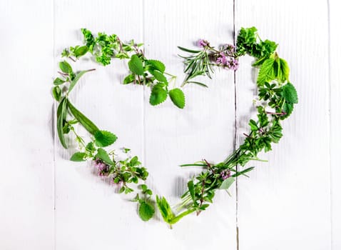 Heart shaped frame of assorted sprigs of fresh green culinary herbs arranged on a rustic white wooden background symbolic of love and romance with central copyspace