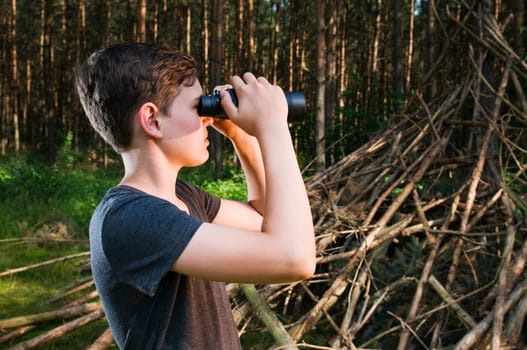 Side head-and-shoulder view of a 13-year-old male teenager looking through binoculars in the woods