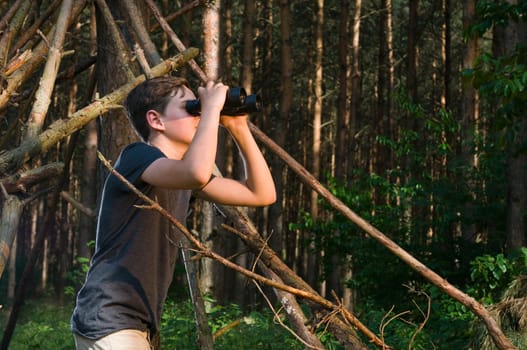 Side-body view of a 13-year-old male teenager looking through binoculars in the woods