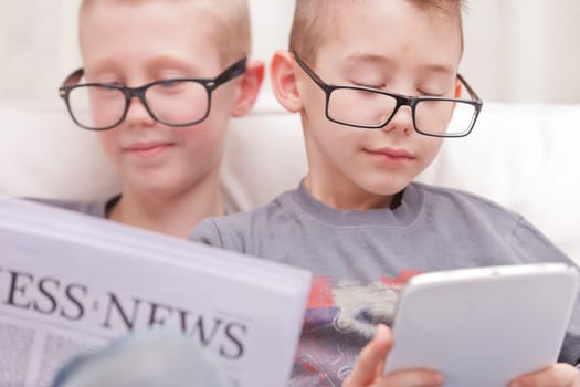 two little boys reading on newspapers or digital devices