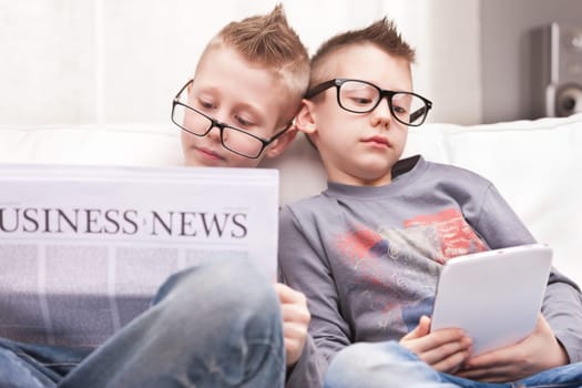 two little boys reading on newspapers or digital devices