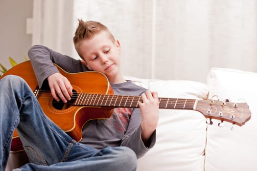 little boy playing guitar on a sofa in his living room
