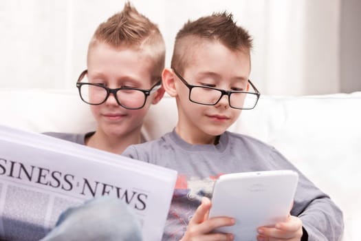 two little boys reading on newspapers or digital devices