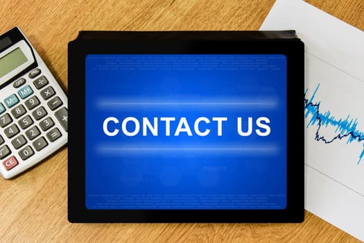 contact us word on digital tablet with calculator and financial graph