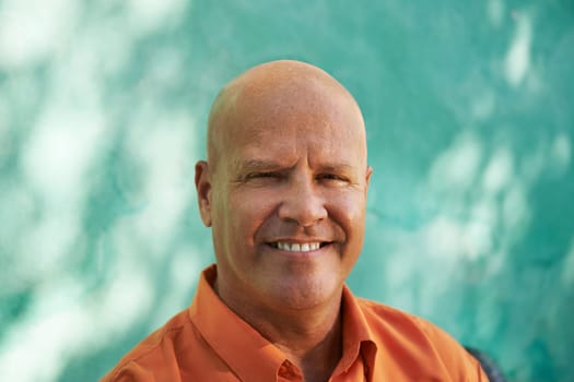 Portrait of mature caucasian man with orange shirt sitting in park and looking at camera with happy expression