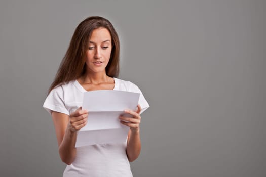 brunette young woman realizes that something GOOD happened reading a white letter or document