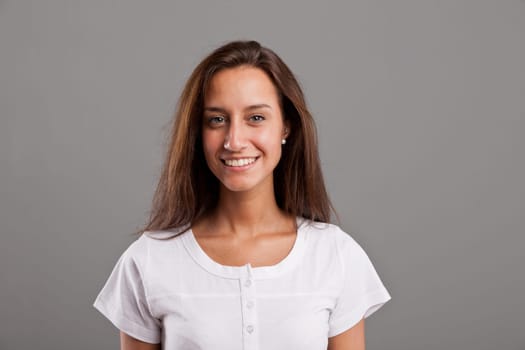 horizontal portrait of a young simple woman smiling sincerely and watching at camera, on a grey neutral background