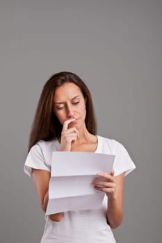 brunette girl reading uncertain news on a white document on a neutral gray faded background
