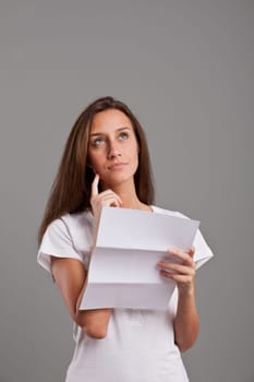 brunette girl thinking about news she received on a white document on a neutral gray faded background