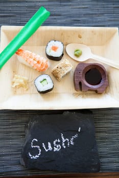 Closeup of plate of sushi with soy sauce and hot wasabi paste and fresh ginger and decorative stone label with text