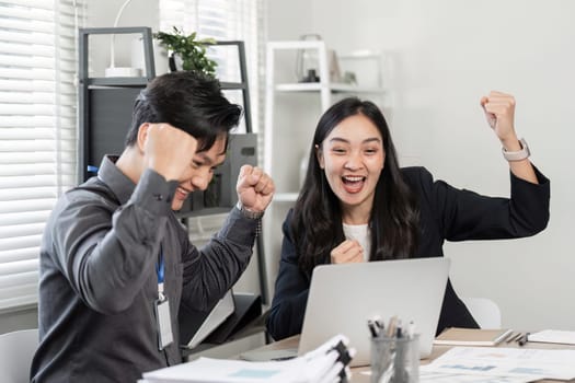 A diverse team of business partners expressing excitement and celebrating their victory while working on a laptop in a bright office environment.