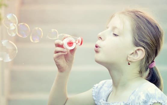 Retro styled photo of young girl blowing soap bubbles