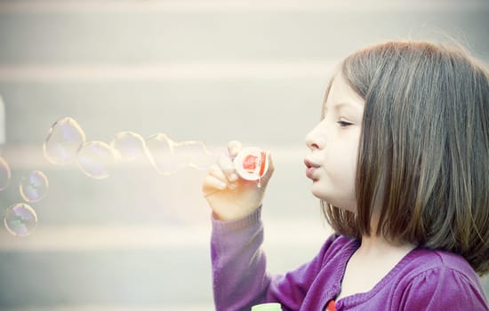 Retro styled photo of young girl blowing soap bubbles