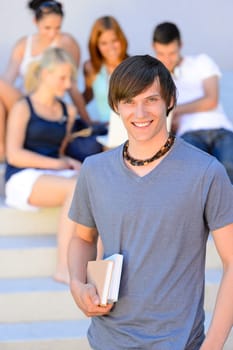 Smiling college student boy holding books friends in background summer