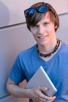 Happy student boy with tablet looking at camera against wall