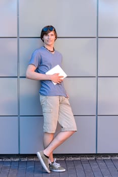 Confident college student boy with tablet standing full length
