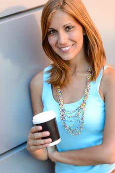 Smiling student girl holding coffee cup summer leaning against wall