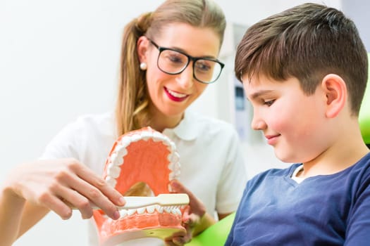 Female dentist explaining boy cleaning tooth with toothbrush on model