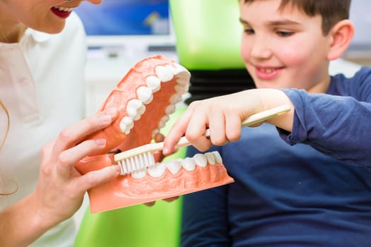 Female dentist explaining boy cleaning tooth with toothbrush on model