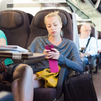 Thoughtful young lady surfing online on smartphone while traveling by train.