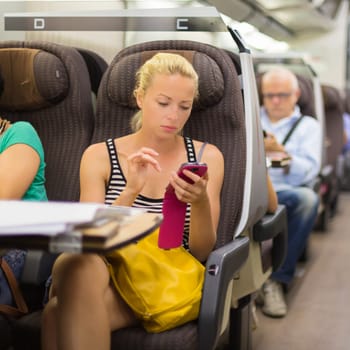 Thoughtful young lady surfing online on smartphone while traveling by train.