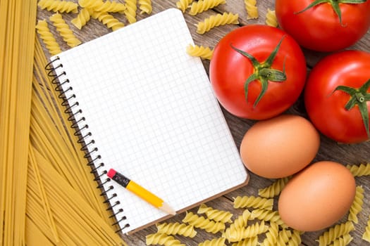 Tomatoes, eggs, uncooked pasta and blank recipe book