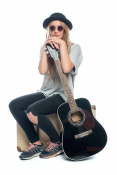 Blonde girl with hat sits on a suitcase and waits