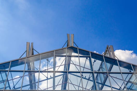 Glass roof in a steel structure in front of a blue sky with clouds.