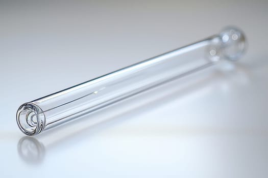 A clear glass tube rests on a white surface, capturing light and showcasing its sleek design and transparent quality.