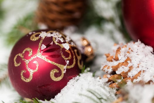 red Christmas baubles between cones and fir branches covered with snow as macro detail