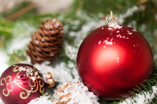 red Christmas baubles between cones and fir branches covered with snow as macro detail