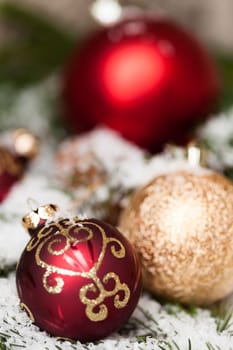 red Christmas baubles between cones and fir branches covered with snow as macro detail