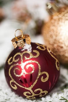 red Christmas baubles between cones and fir branches covered with snow as macro detail