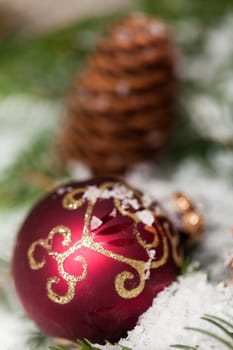 red Christmas baubles between cones and fir branches covered with snow as macro detail