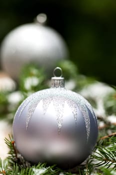 Silver Christmas tree balls in green fir branches with white shiny snow as macro detail