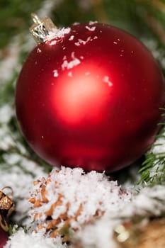 red Christmas baubles between cones and fir branches covered with snow as macro detail